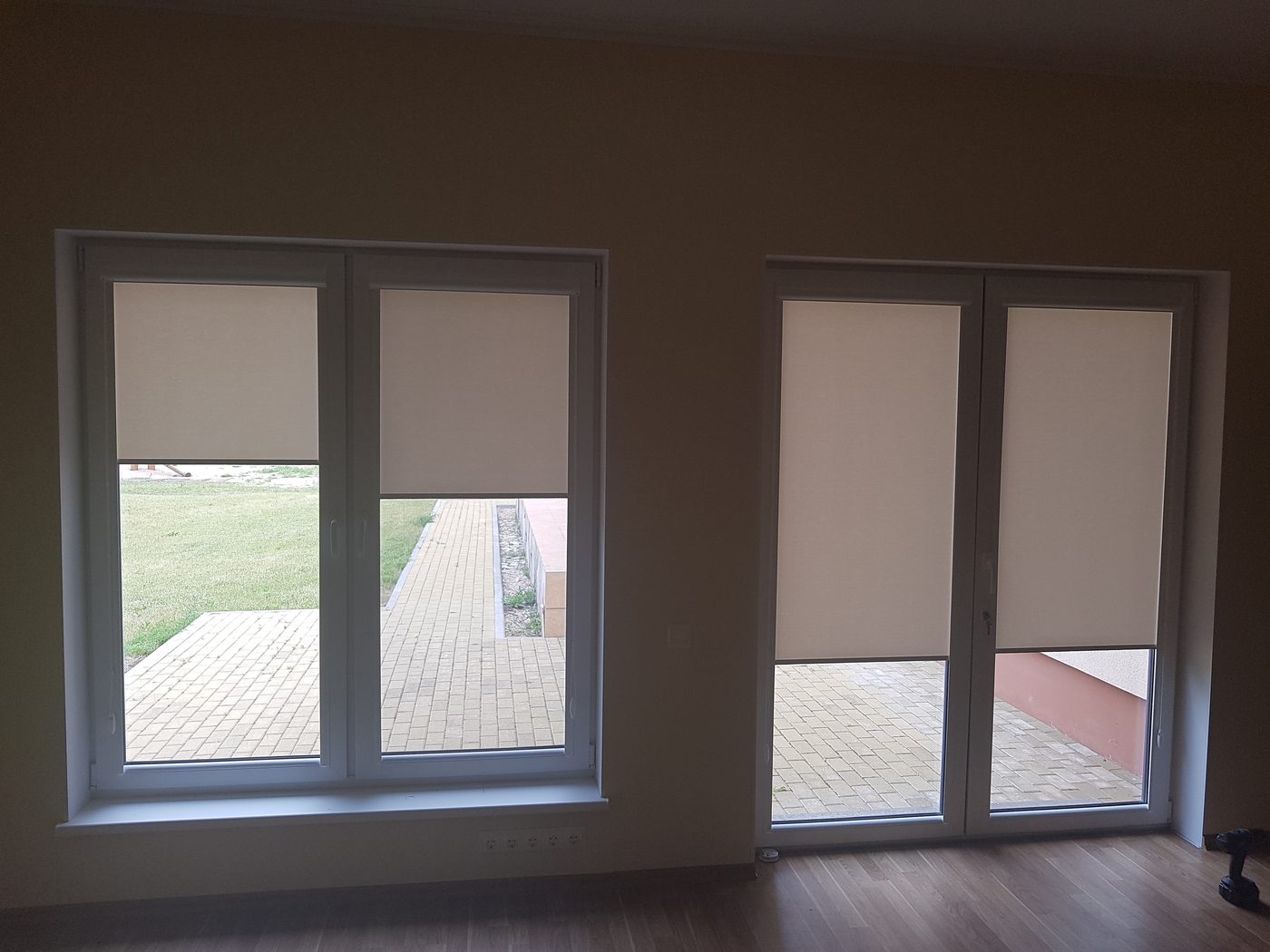 Baltas kasešu žalūzijas viesistabas logā un balkona durvīs Baltas kasešu žalūzijas viesistabas logā un balkona durvīs