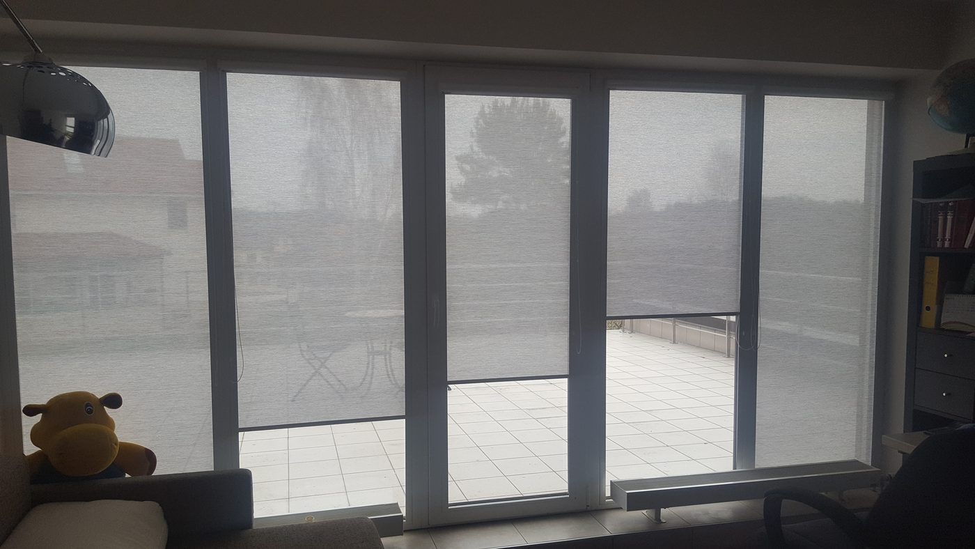 Pelēkas screen kasešu žalūzijas uz panorāmas durvīm ar izeju uz terasi Pelēkas screen kasešu žalūzijas uz panorāmas durvīm ar izeju uz terasi