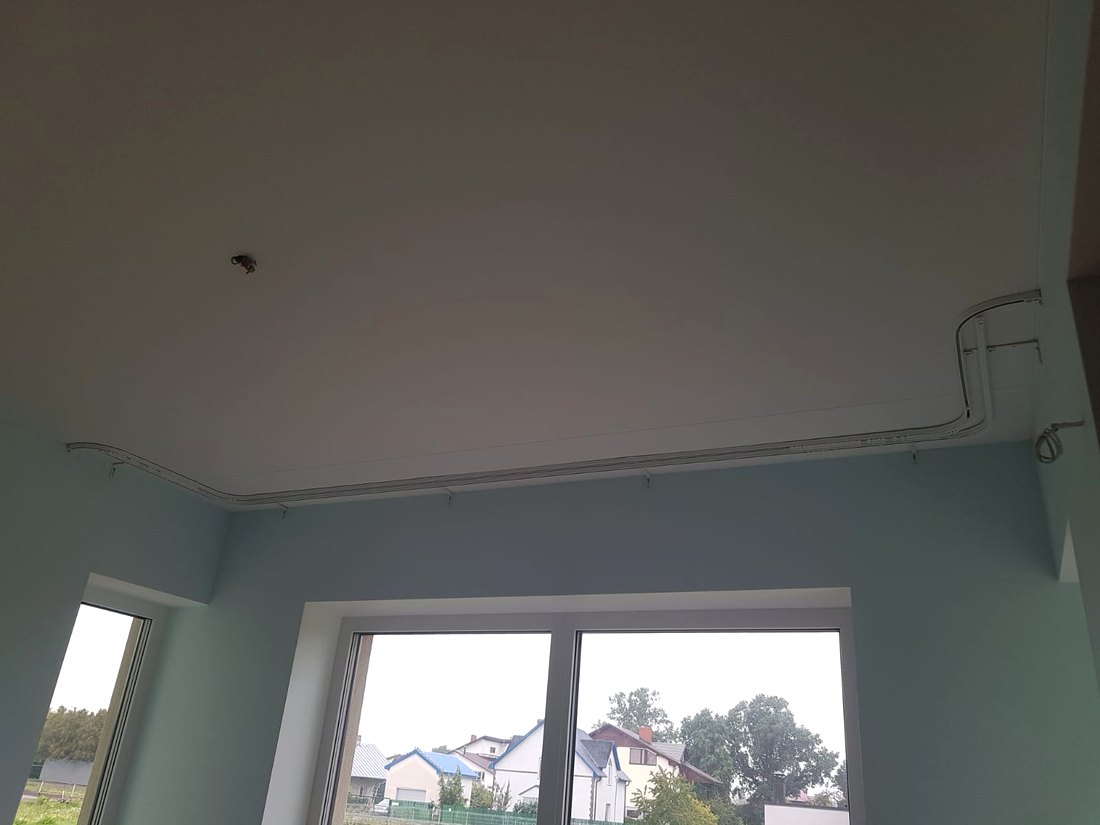 Balta griestu profila karnīze ar liektiem pagriezieniem gar erkera perimetru ar panorāmas logu