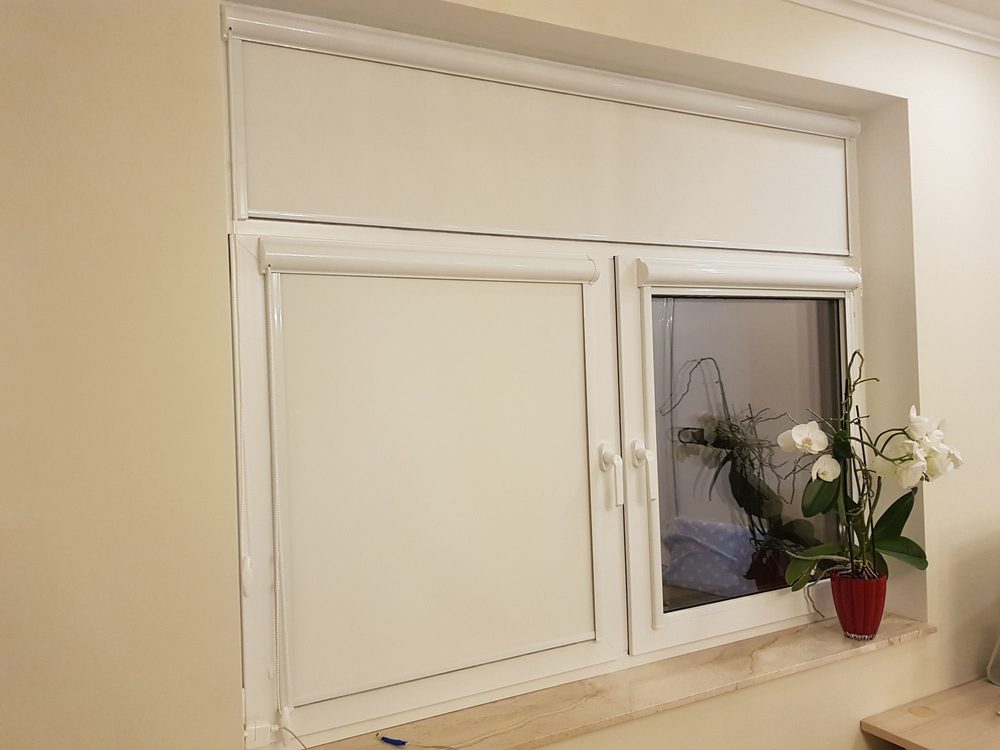 Baltas kasešu žalūzijas logā ar augšējo vērtni